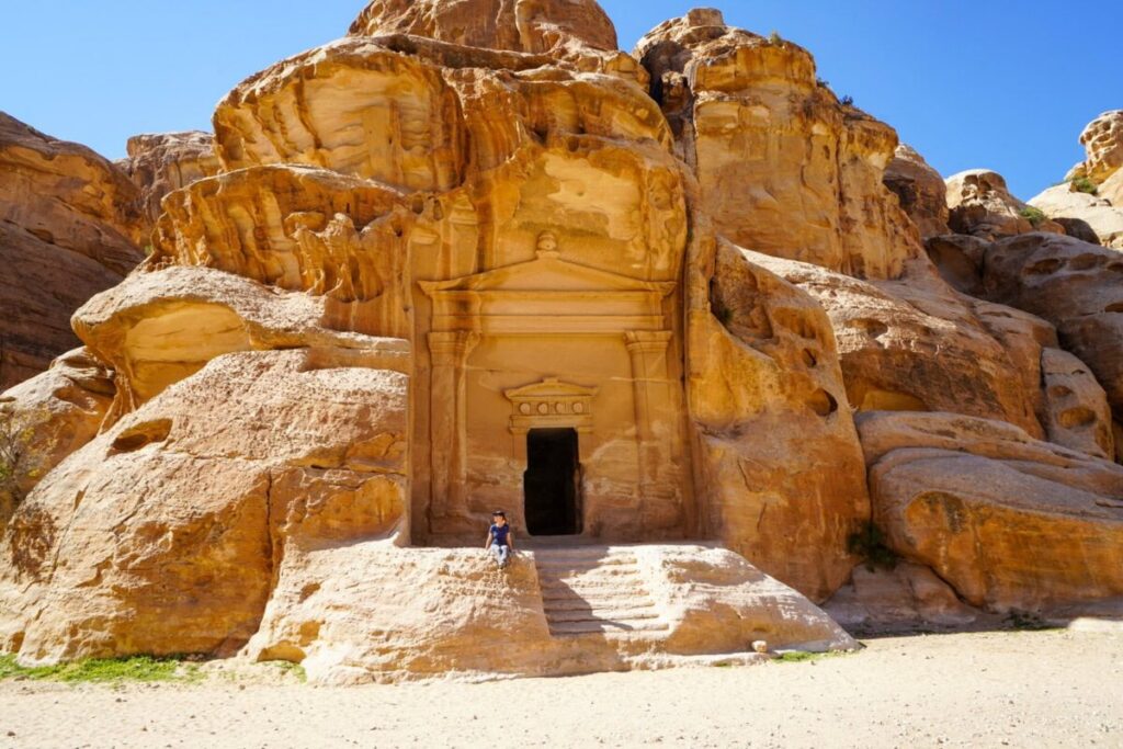 a girl sit at sunny Entrance to the rock carvings of Petra Caves